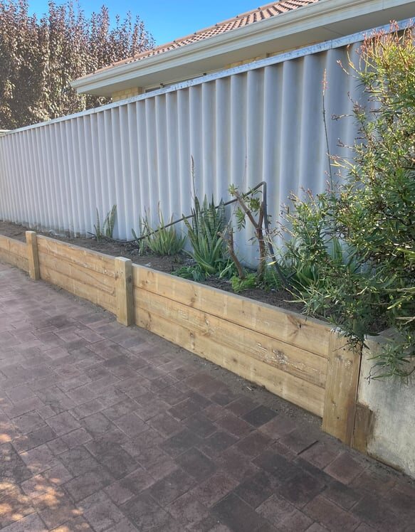 New timber garden retaining bed beside a boundary fence